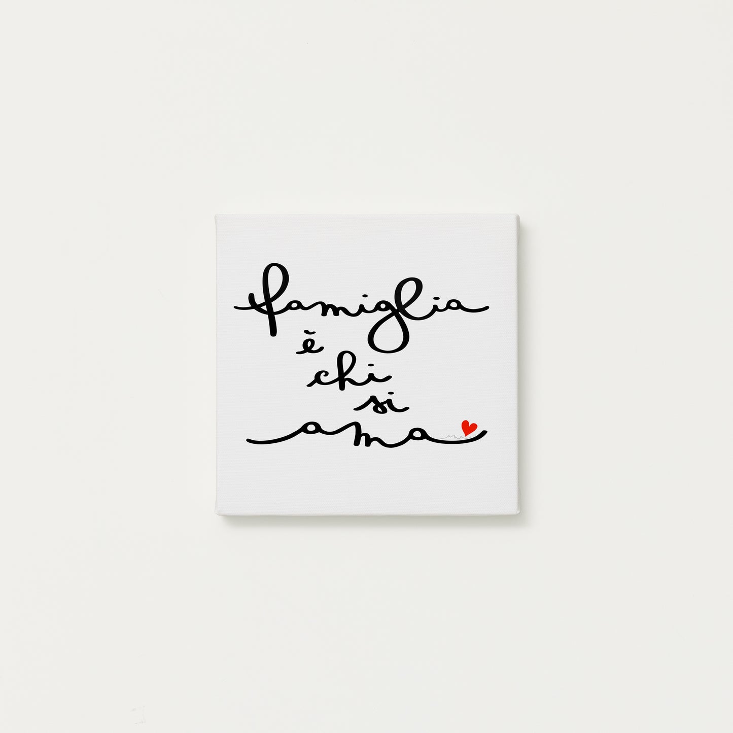 tela calligrafata con la scritta “famiglia è chi si ama” scritta a mano in corsivo nero con un piccolo cuore rosso - formato quadrato cm 20x20