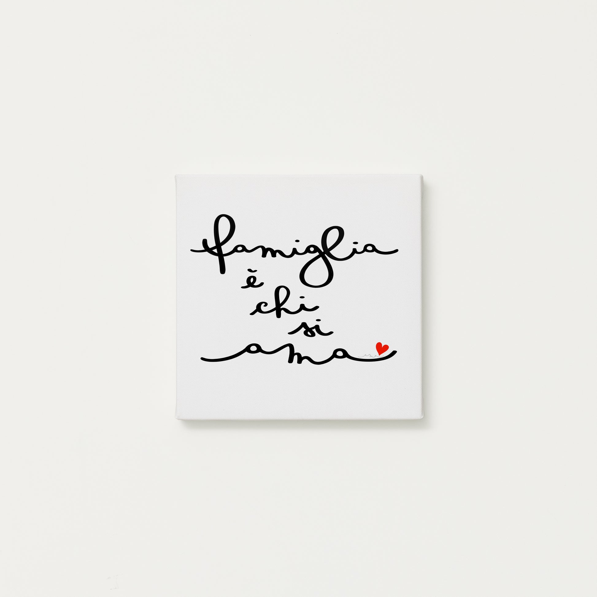tela calligrafata con la scritta “famiglia è chi si ama” scritta a mano in corsivo nero con un piccolo cuore rosso - formato quadrato cm 20x20