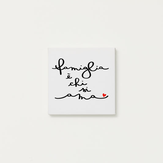 tela calligrafata con la scritta “famiglia è chi si ama” scritta a mano in corsivo nero con un piccolo cuore rosso - formato quadrato cm 20x20