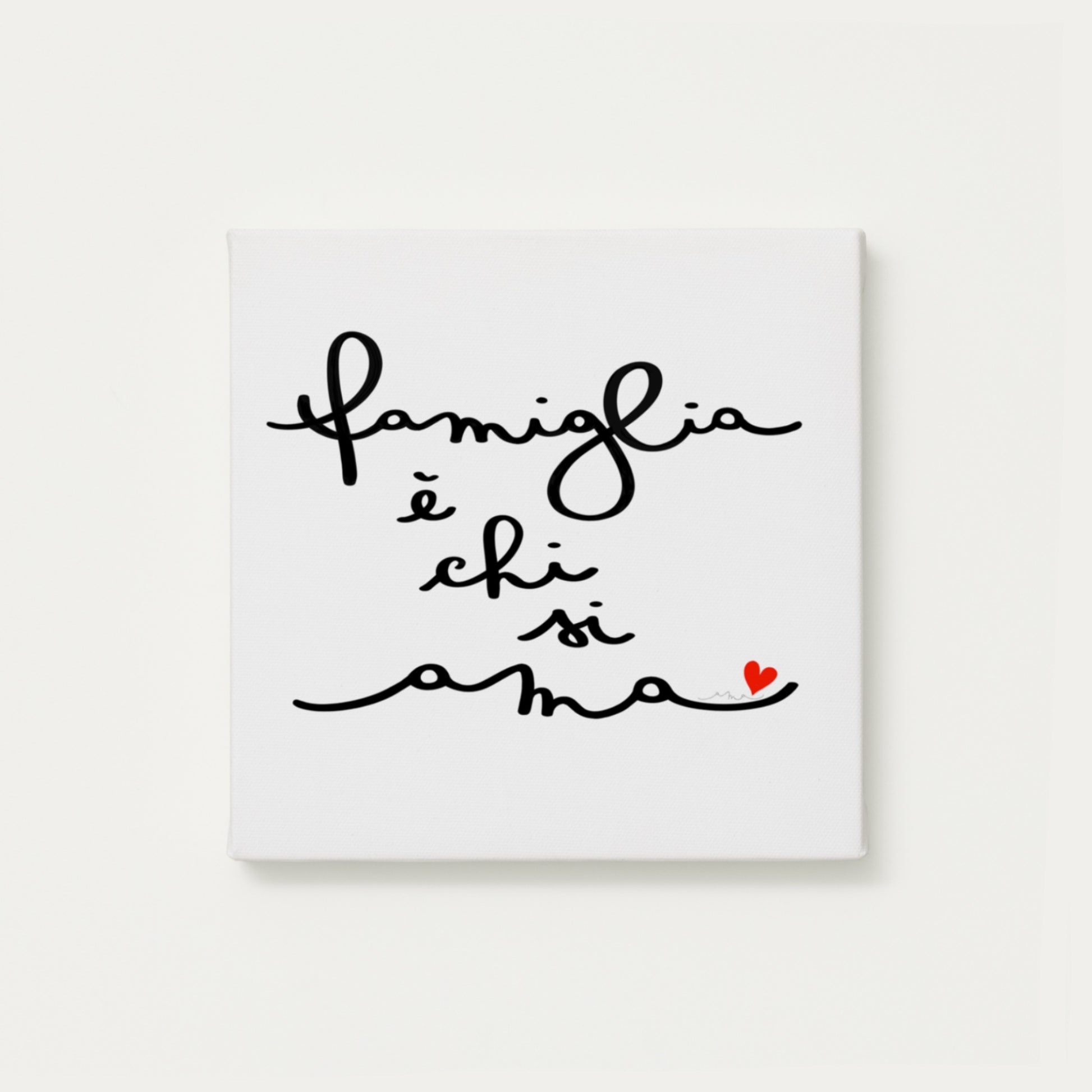 tela calligrafata con la scritta “famiglia è chi si ama” scritta a mano in corsivo nero con un piccolo cuore rosso - formato quadrato cm 30x30