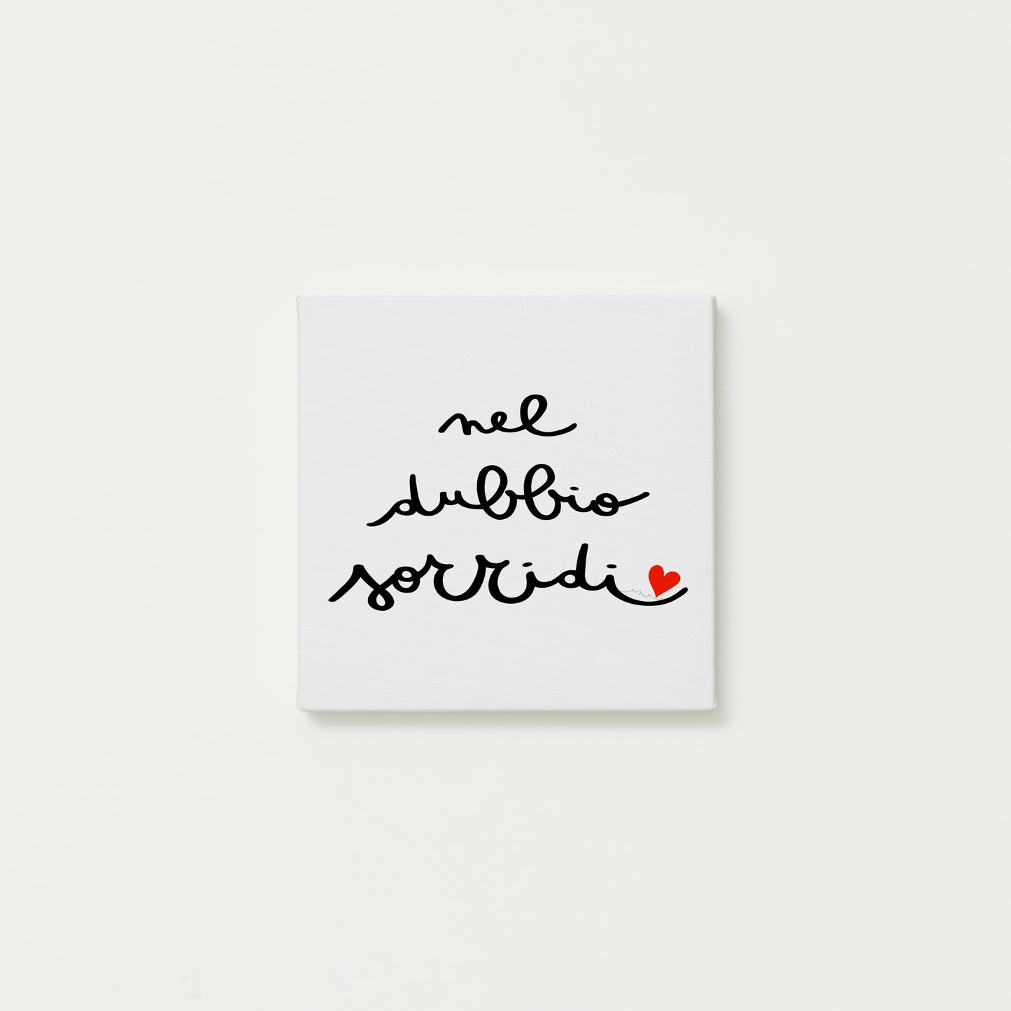 tela calligrafata con la scritta “nel dubbio sorridi” scritta a mano in corsivo nero con un piccolo cuore rosso - formato quadrato cm 20x20
