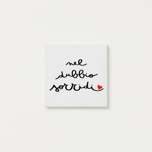 tela calligrafata con la scritta “nel dubbio sorridi” scritta a mano in corsivo nero con un piccolo cuore rosso - formato quadrato cm 20x20
